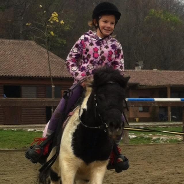 A smiling young rider in a helmet on a black and white pony in an arena